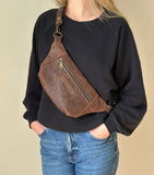 Person wearing a brown leather sling bag over one shoulder against a beige background