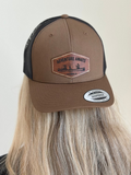 Brown and black cap with 'Adventure Awaits' leather patch on a plain background